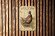 A vintage-style sign for a ring-necked pheasant rooster is displayed on a wooden wall.