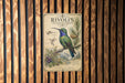 a vintage-style metal sign with illustrations of a hummingbird and pine trees, mounted on a wooden wall.