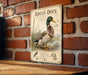 a metal sign with an illustration of a roan duck, mounted on a brick wall.