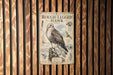 a metal sign with a picture of a rough-legged hawk and text, mounted on a wooden wall.