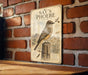 a vintage-style metal sign with a bird illustration, mounted on a brick wall.