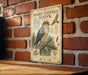 a metal sign with a picture of a sharp-shinned hawk, mounted on a brick wall.
