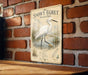 A vintage-style illustration of a snowy egret wading in a marsh, mounted on a brick wall.