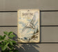 a vintage-style sign depicting a snowy owl in flight, mounted on a wall next to a plant.