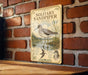 A vintage-style metal sign with illustrations and text, mounted on a brick wall.