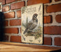 a vintage-style metal sign with a detailed illustration of a pine grouse, mounted on a brick wall.