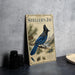 a vintage-style metal sign with a blue jay illustration, placed on a countertop next to some black camera lenses.
