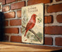 A vintage-style metal sign with a red bird perched on a branch, mounted on a brick wall.