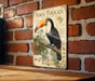 A vintage-style poster of a toucan is displayed on a brick wall, featuring a detailed illustration of the bird perched on a branch with various tropical plants and fruits.