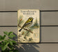 A metal sign with a bird illustration and text, mounted on a wall next to a plant.