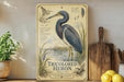 A framed illustration of a blue heron, labeled as a "Tricolored Heron" and featuring detailed illustrations of the bird and its natural habitat.