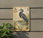 a sign with a detailed illustration of a blue heron, surrounded by plants and a wooden structure.