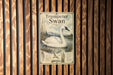 A vintage-style metal sign with an illustration of a white swan in a pond, mounted on a wooden wall.