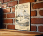 A vintage-style metal sign featuring illustrations of two swans swimming in a pond, mounted on a brick wall.