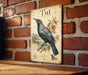 a vintage-style metal plaque with a detailed illustration of a blue and green bird perched on a branch, set against a brick wall.