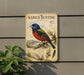 a vintage-style metal sign with a colorful illustration of a bird perched on a branch, surrounded by various plant life.