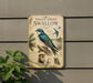 a vintage-style metal sign with illustrations and text about a violet-green swallow, mounted on a wall next to a plant.