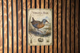 a vintage-style metal sign with a bird illustration, mounted on a wooden wall.