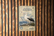 a poster of a wandering albatross, which is a large seabird that is known for its long flights and impressive wingspan. The poster is displayed on a wooden wall, and it appears to be a collage of multiple images. The poster includes a detailed illustration of the albatross, along with text that provides information about the species, such as its size, habitat, and behavior. The poster also includes a compass rose and a map, which are used to help locate the albatross in the vast ocean.