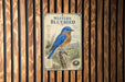A metal sign with a blue bird illustration is mounted on a wooden wall.