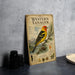 A vintage-style poster or book titled "Western Tanager" featuring a colorful illustration of a tanager bird perched on a branch with pine cones and other natural elements.