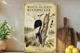 a vintage-style poster of a white-headed woodpecker on a tree branch, surrounded by illustrations of pine trees and other wildlife. The poster is displayed on a shelf next to a wooden cutting board and a potted plant.