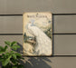a vintage-style metal sign with a white peacock illustration, mounted on a wall.
