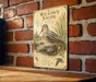 A vintage-style metal sign featuring an illustration of a bird, likely Wilson's Snipe, mounted on a brick wall.