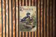 A vintage-style metal sign with an illustration of two wood ducks on a log, mounted on a wooden wall.