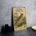 A vintage-style metal sign with a detailed illustration of a wood thrush bird, placed on a gray countertop next to some black camera lenses.