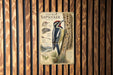 A metal plaque with an illustration of a yellow-bellied sapsucker perched on a tree trunk, surrounded by pine needles and a map of the region.