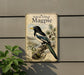 a vintage-style sign with a black and white illustration of a magpie perched on a branch, surrounded by various natural elements such as pine cones and leaves.