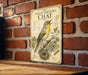 A vintage-style metal sign with a yellow-breasted chat bird illustration is mounted on a brick wall.