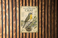 A vintage-style metal sign with a yellow-breasted chat bird illustration is mounted on a wooden wall.