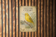 A vintage-style poster of a yellow canary is displayed on a wooden wall, featuring an illustration of the bird perched on a branch.