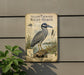 a vintage-style metal sign with a detailed illustration of a yellow-crowned night-heron, mounted on a wall.