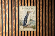 A vintage-style illustration of a yellow-eyed penguin is displayed on a wooden wall, accompanied by text that provides information about the species.