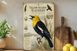A vintage-style poster of a yellow-headed blackbird is displayed on a shelf, accompanied by a potted plant, a wooden cutting board, and some lemons.