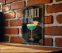 A framed poster of a cocktail called "Acapulco" is displayed on a brick wall, featuring a stylized illustration of a tequila-based drink with a pineapple garnish.