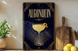 A framed poster of a cocktail called Algonquin, featuring a glass of the drink with a lemon twist, is displayed on a wall next to a wooden cutting board and a potted plant.