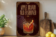 a decorative sign with the text "APPLE BRANDY OLD FASHIONED" and an illustration of a glass of amber-colored liquid with a slice of apple on the rim.