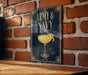 A sign with the text "ARMY & NAVY" and an illustration of a cocktail glass is displayed on a brick wall.