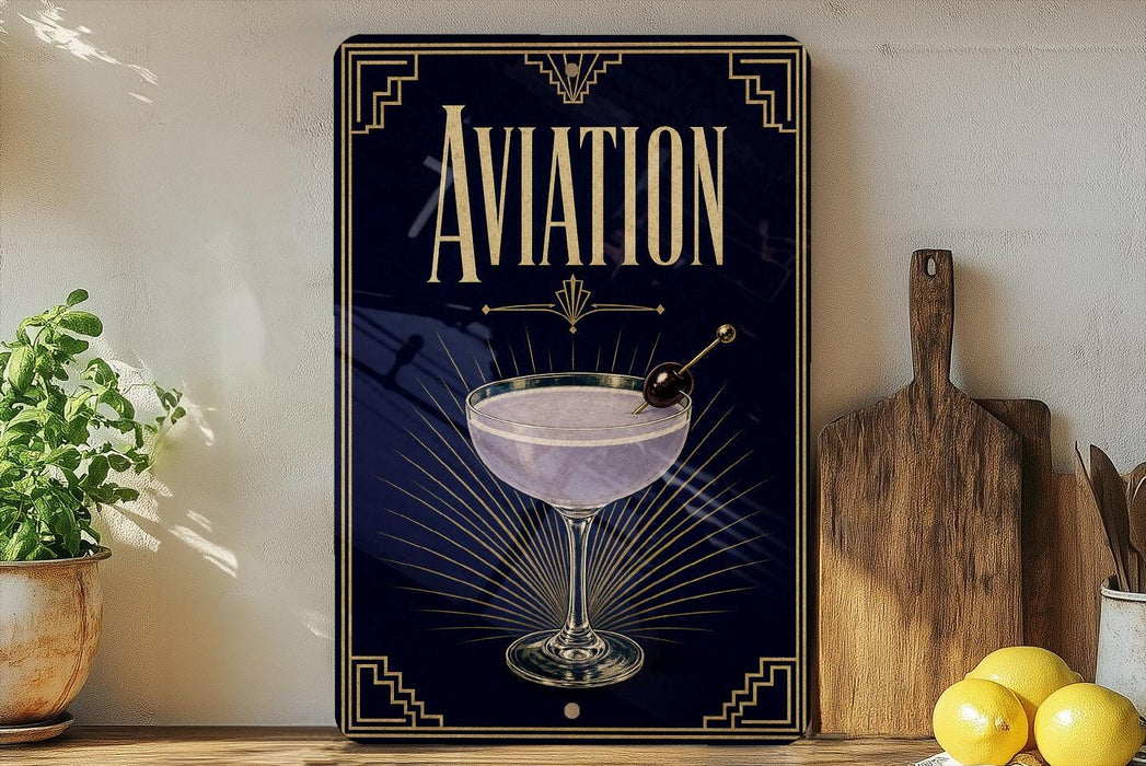 a decorative sign with the word "AVIATION" prominently displayed, along with an illustration of a martini glass and a cherry. The sign is placed on a wooden surface, with a potted plant, a cutting board, and some lemons nearby.