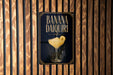 A sign for a banana daiquiri cocktail is displayed on a wooden wall.