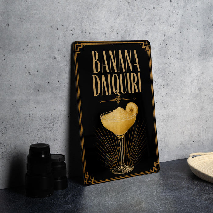 A sign for a banana daiquiri cocktail is displayed on a table, with a stack of black cups and a white dish nearby.