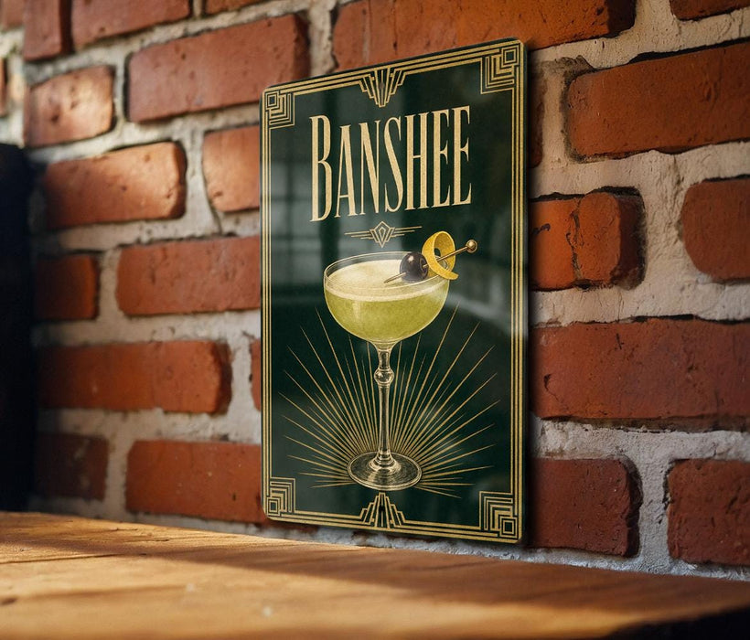 A framed poster of a cocktail with a lemon twist, hanging on a brick wall.