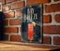 A sign for "Bay Breeze" cocktail is displayed on a brick wall, featuring an illustration of a red drink with a lime garnish.