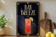 a framed poster advertising a drink called "Bay Breeze" with a glass illustration of a red drink and a lemon slice.
