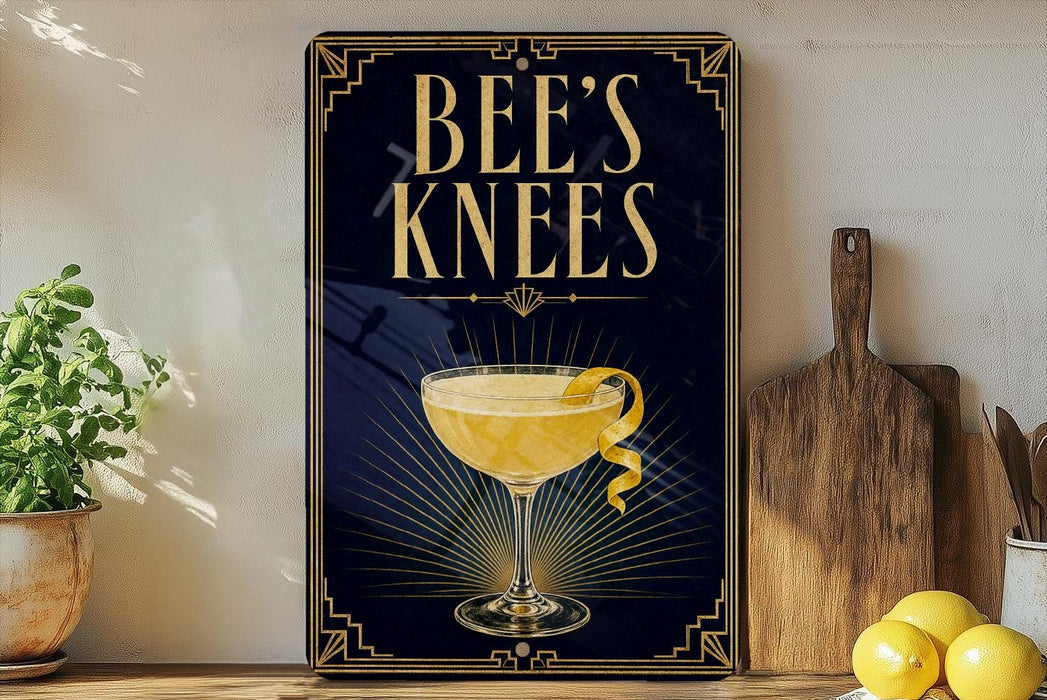 A decorative sign for "Bee's Knees" cocktail, featuring a glass of yellow liquid and a lemon twist, is displayed on a wooden shelf next to a wooden cutting board and a potted plant.