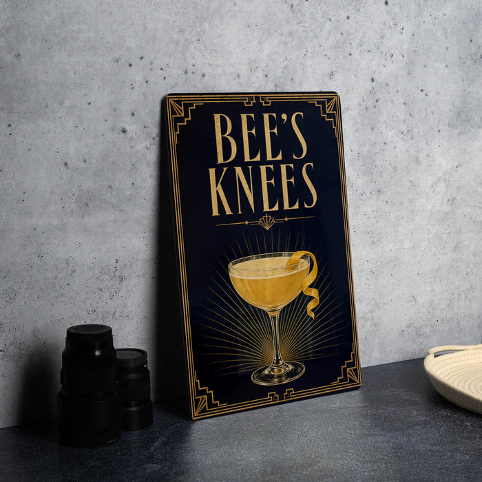 A framed poster with the text "BEE'S KNEEES" and an illustration of a cocktail glass with a lemon twist.